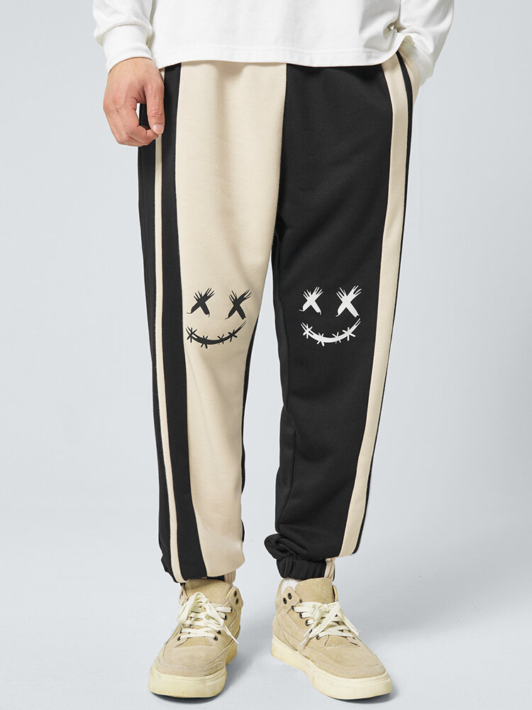 Pantalones de chándal sueltos con puños y patchwork en contraste con estampado de cara sonriente para hombre
